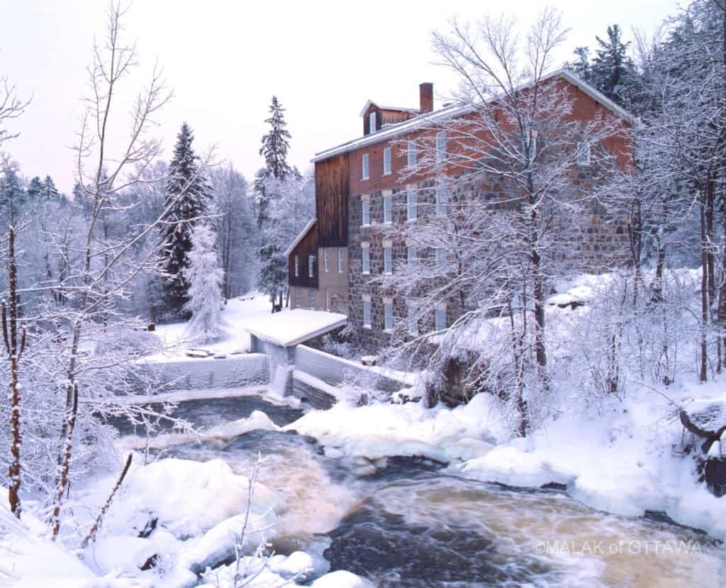 Snow-covered historic building by a flowing river in Ottawa during winter.