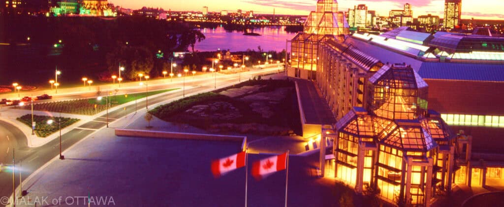 Night view of Malak of Ottawa with illuminated glass structure and flags, near the National Gallery.
