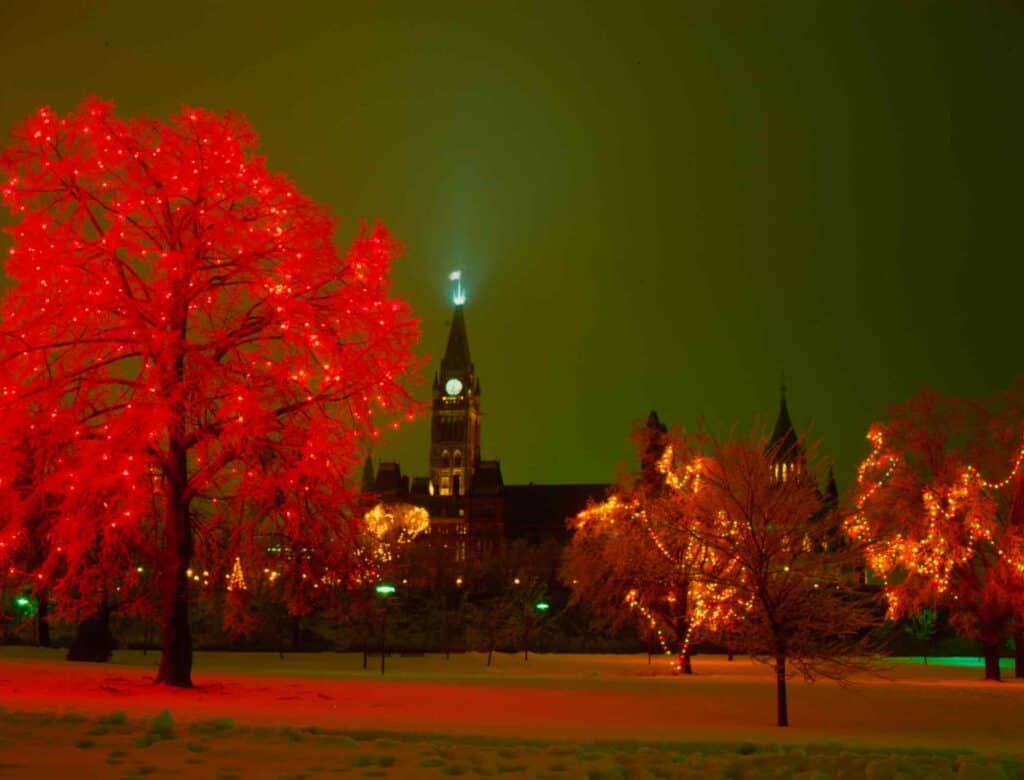 Night view of Ottawa with glowing autumn trees and Parliament Hill in the background.