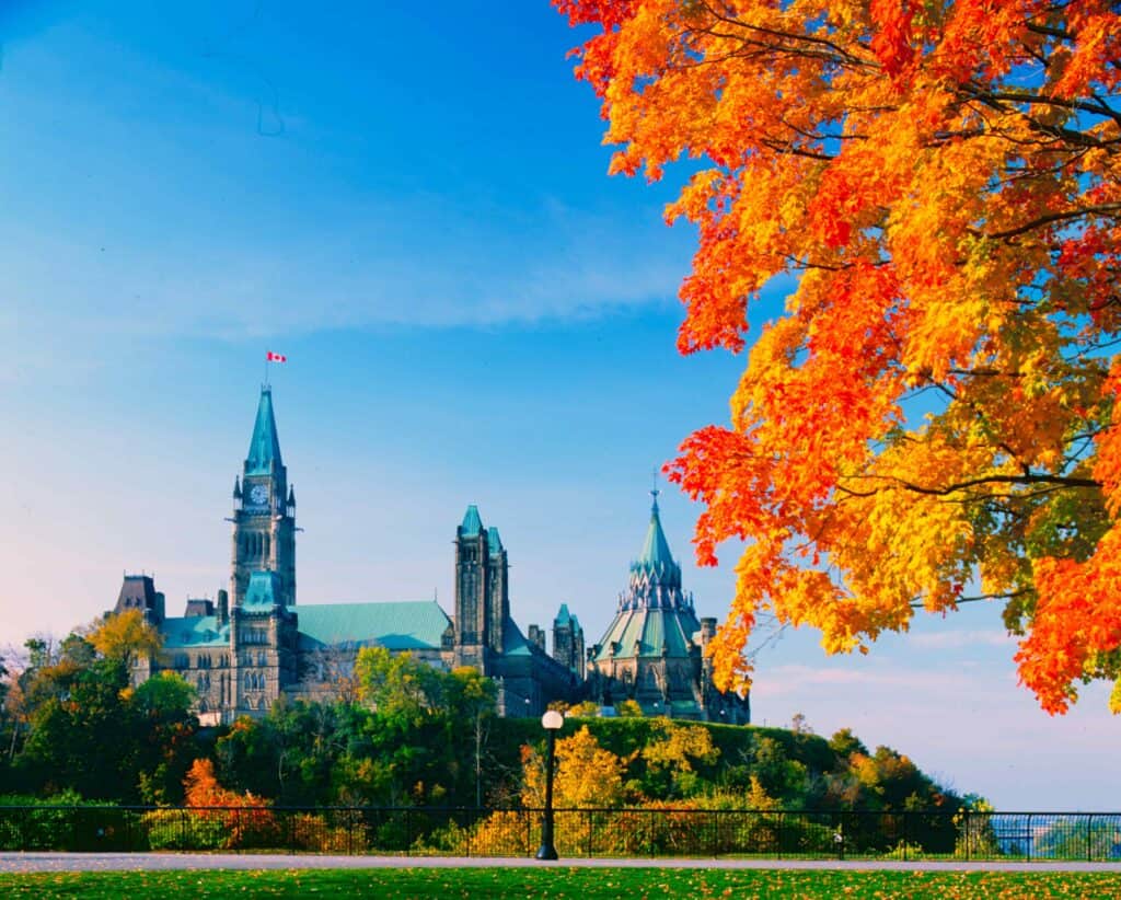 Ottawa Parliament Buildings with vibrant autumn foliage and clear blue sky.