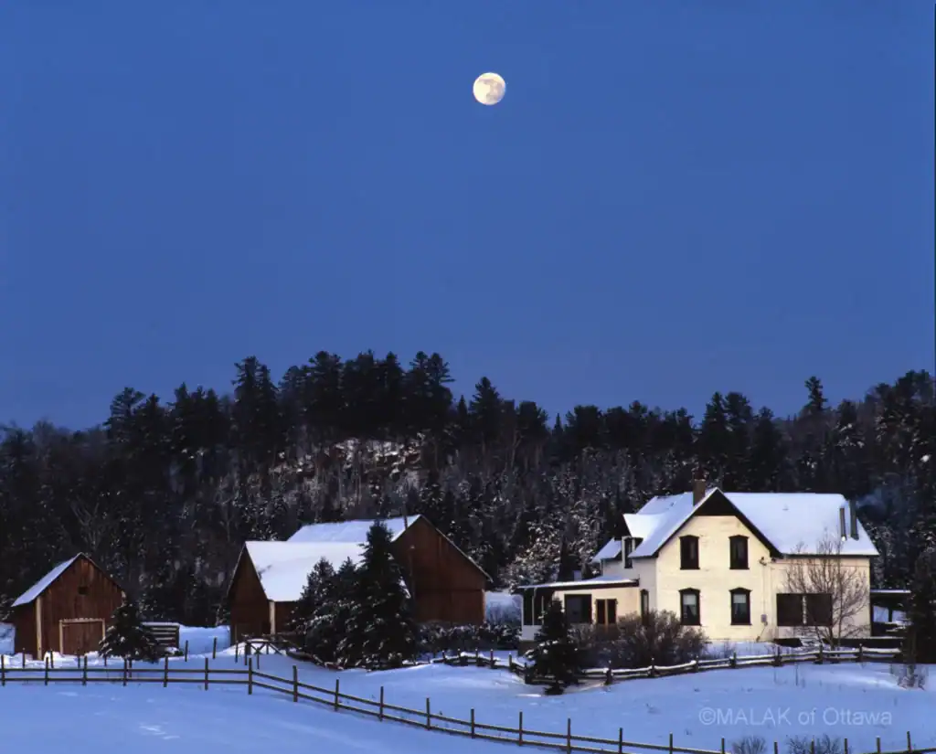 Snow-covered houses under a clear night sky with a visible moon.