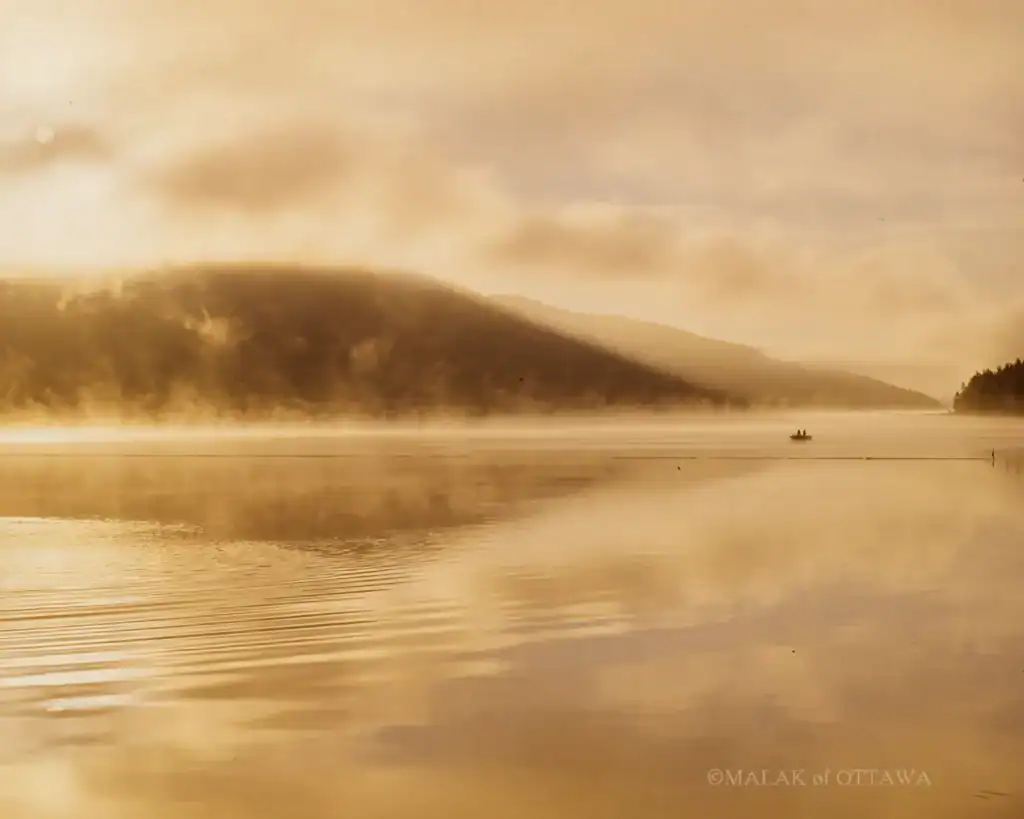 Beautiful sunset over calm lake with misty mountains in the background.