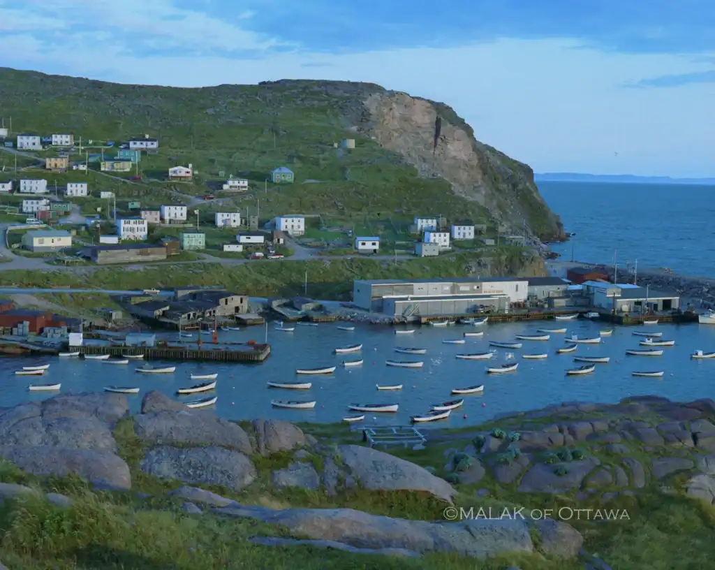 Fishing boats anchored in the harbor at Malak of Ottawa, with colorful houses on the hillside and a.