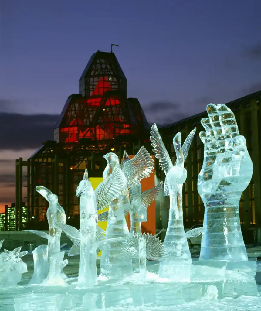 Ice sculpture art installation in Ottawa with illuminated figures and a historic building in the bac.