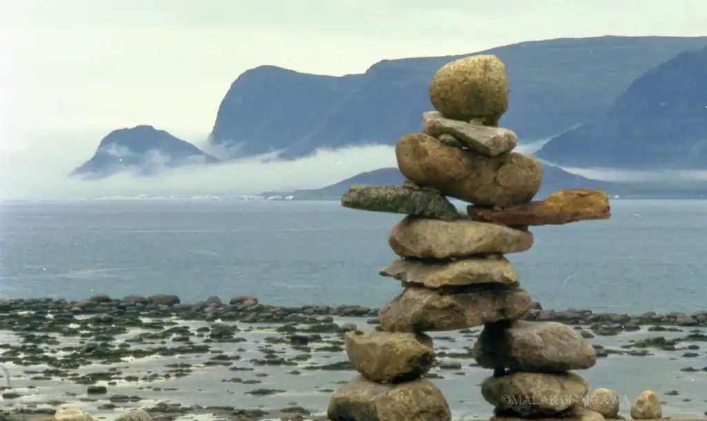 Stone cairn stacked on rocky beach with ocean and misty mountains in the distance.