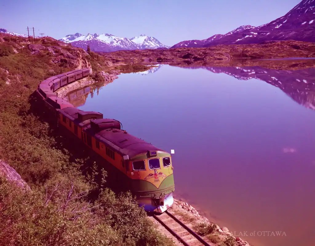 Beautiful train traveling along a lake with mountain backdrop in Ottawa.
