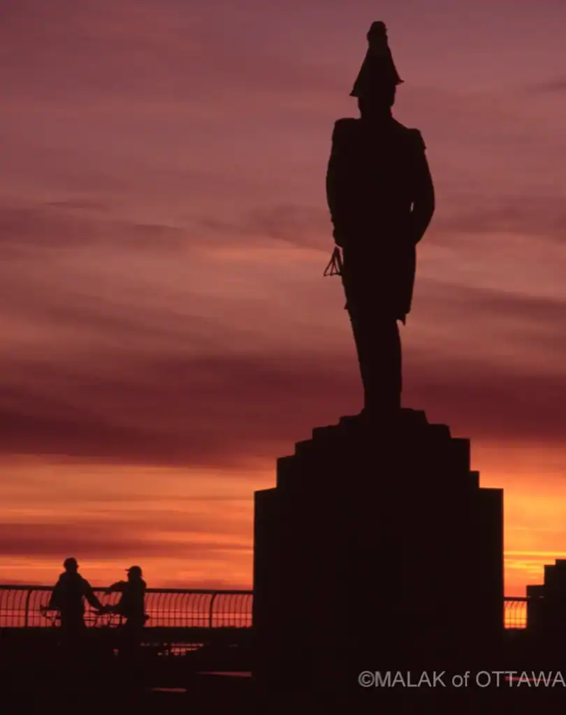 Statue of Malak of Ottawa silhouetted against a colorful sunset sky.