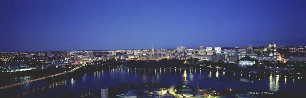 Night view of Ottawa skyline with illuminated buildings and river.